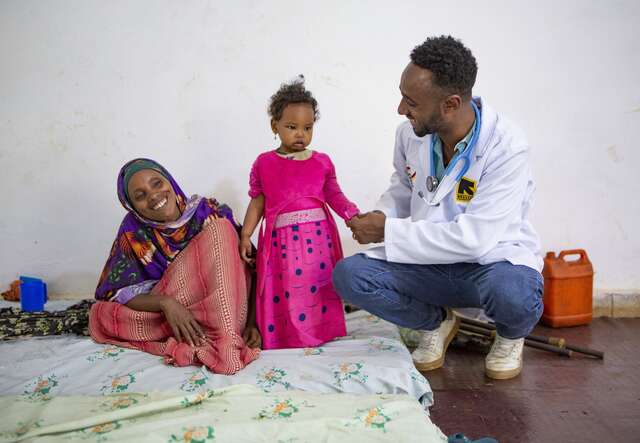 영양실조 치료를 받은 한 어린이가 힘차게 서있고 의료진과 엄마가 환하게 웃으면서 바라보고 있습니다.